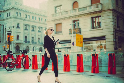 Stylish woman in black outfit walking by bike stand in a European city street.