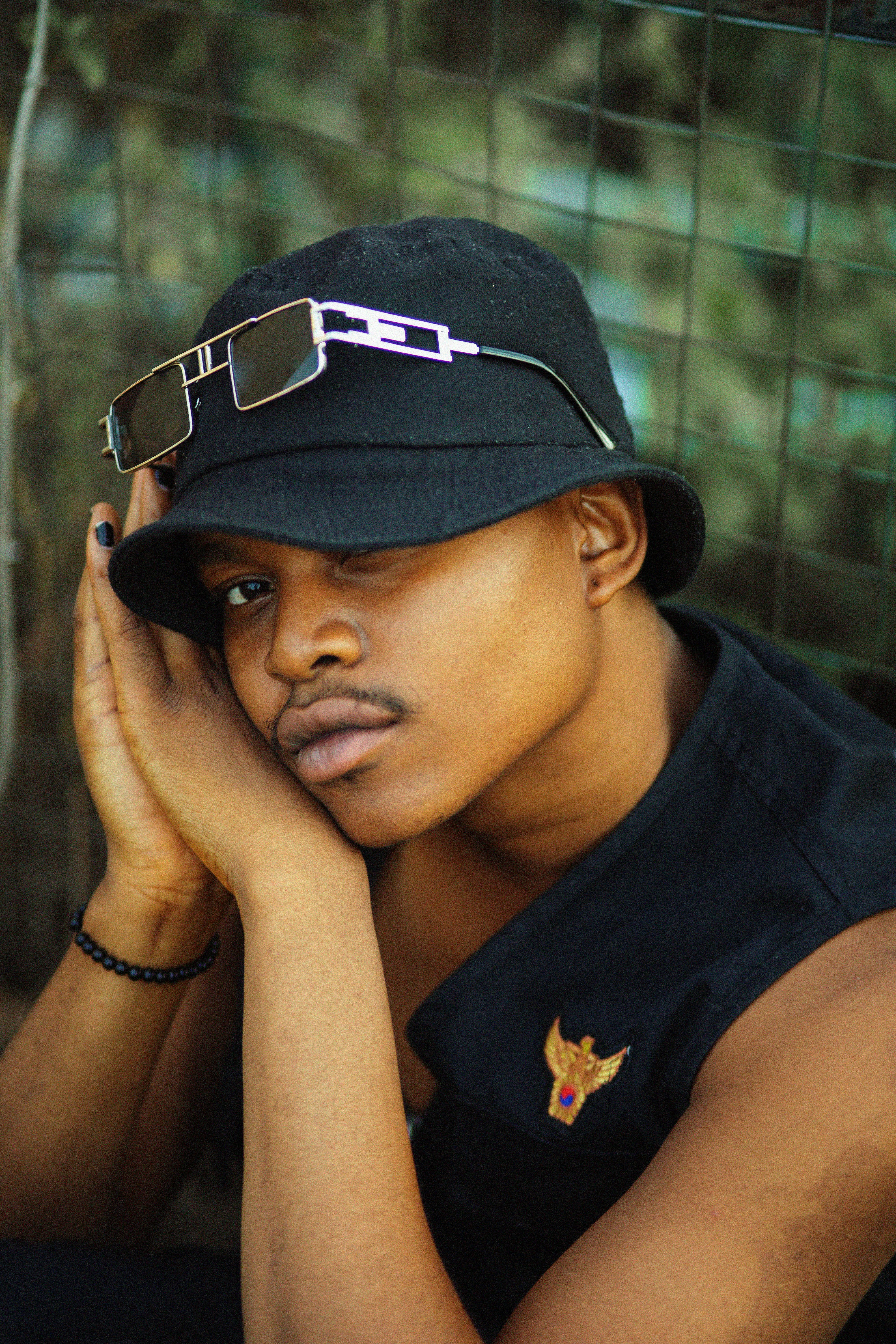 A young man with a trendy look wearing a bucket hat and sunglasses in an outdoor setting.