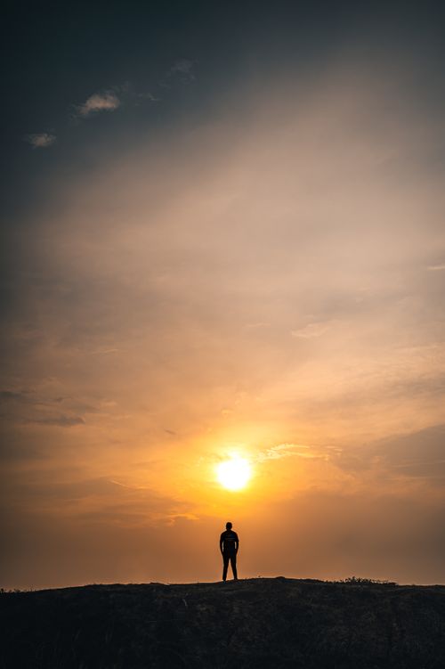 Free A lone man stands silhouetted against a vibrant sunset sky in a peaceful countryside setting. Stock Photo