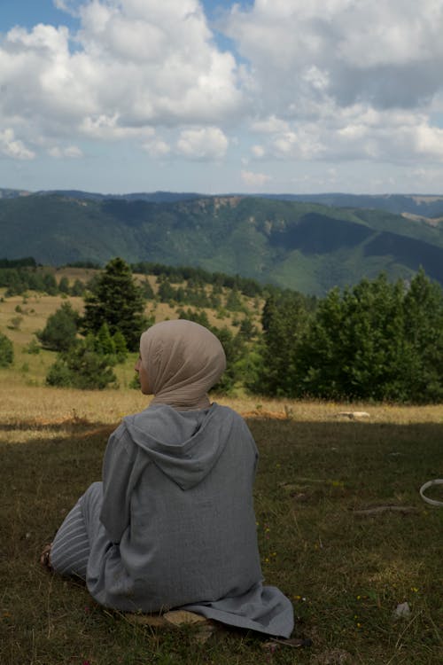 Woman in Hijab Sitting on Hill with Trees behind
