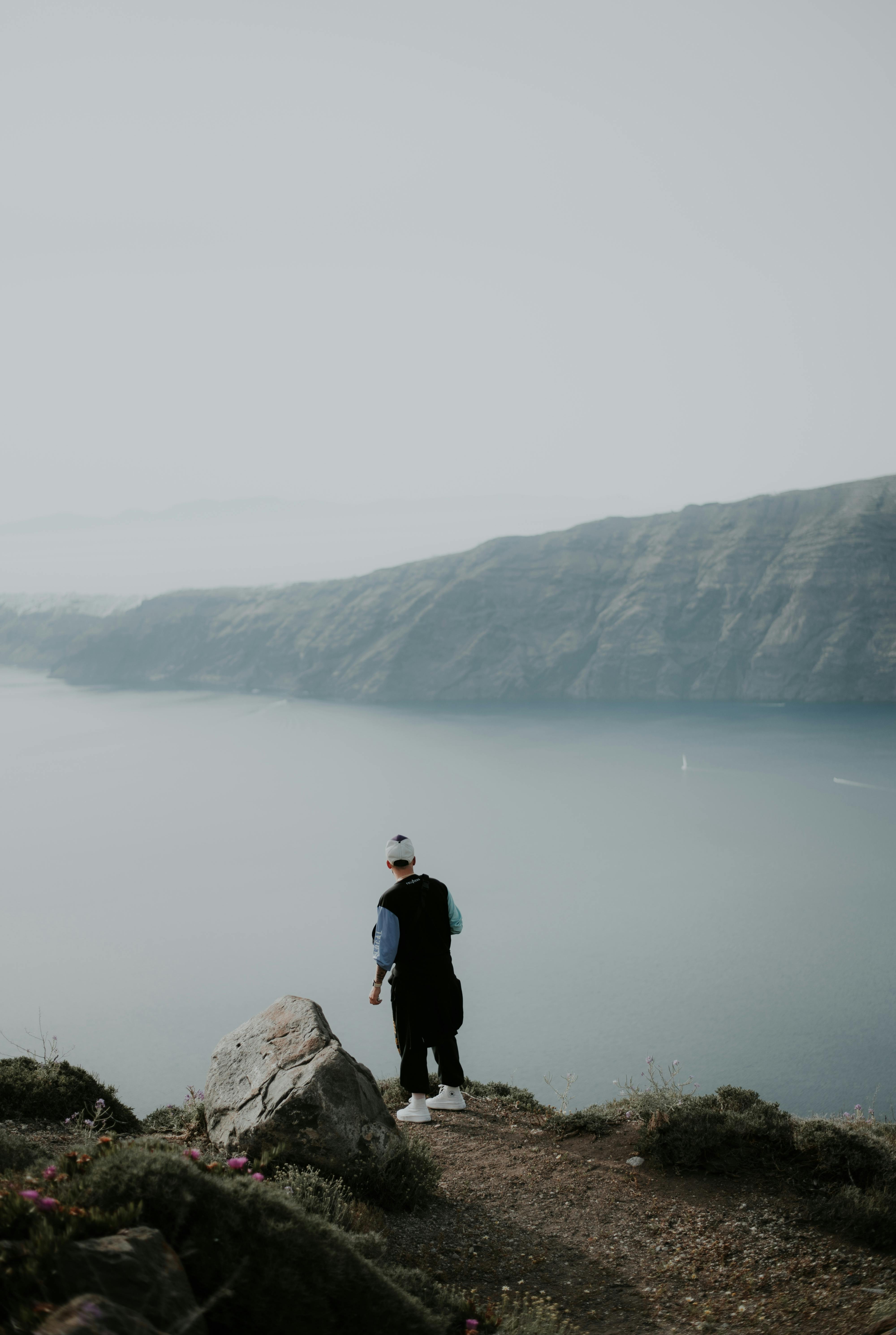 Man standing on a rocky cliff overlooking the sea in a serene Santorini landscape.