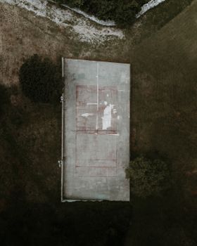 Drone shot capturing a neglected tennis court surrounded by greenery, showcasing decay and nature's reclamation.