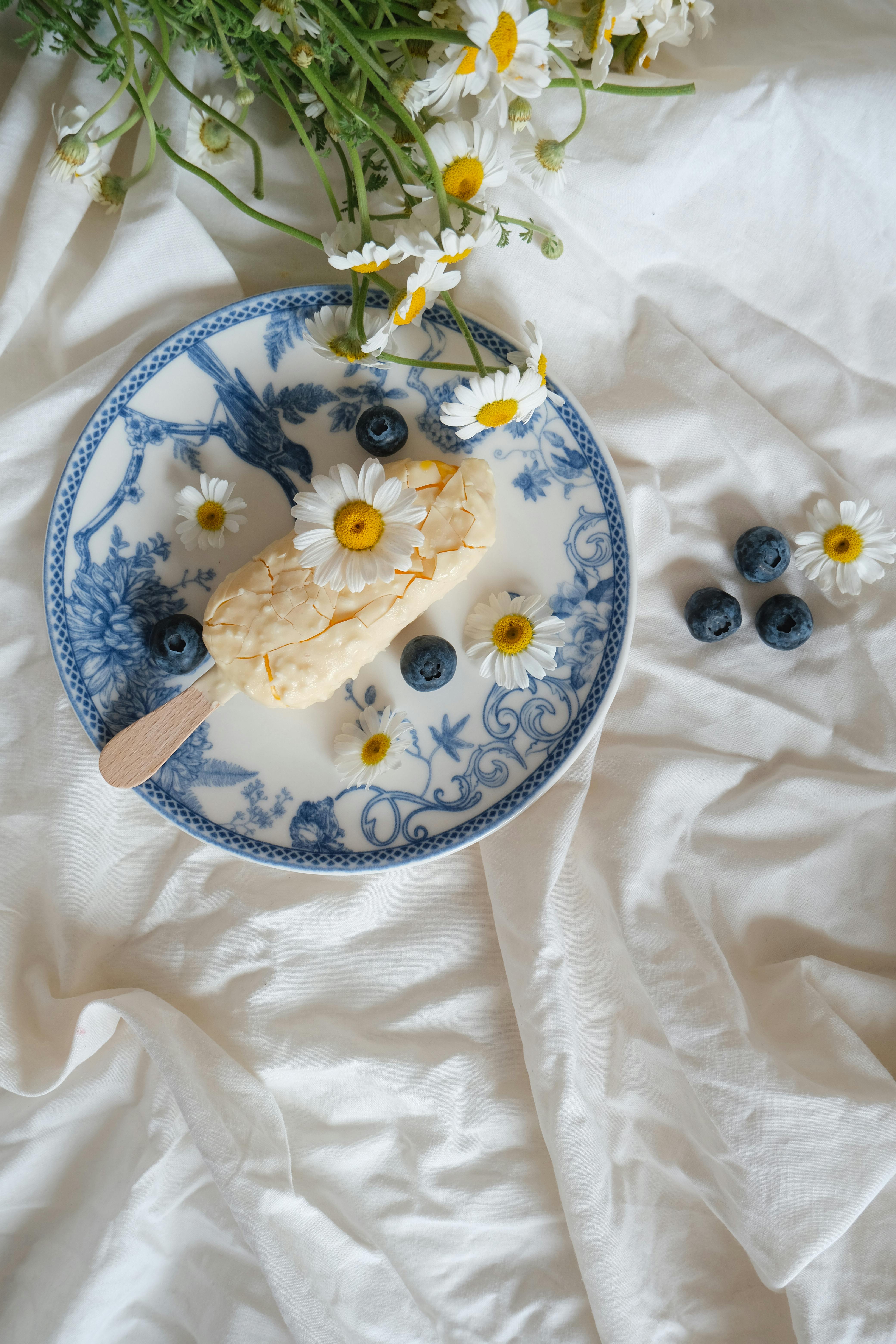 Artistic display of ice cream with blueberries and daisies on a decorative plate.