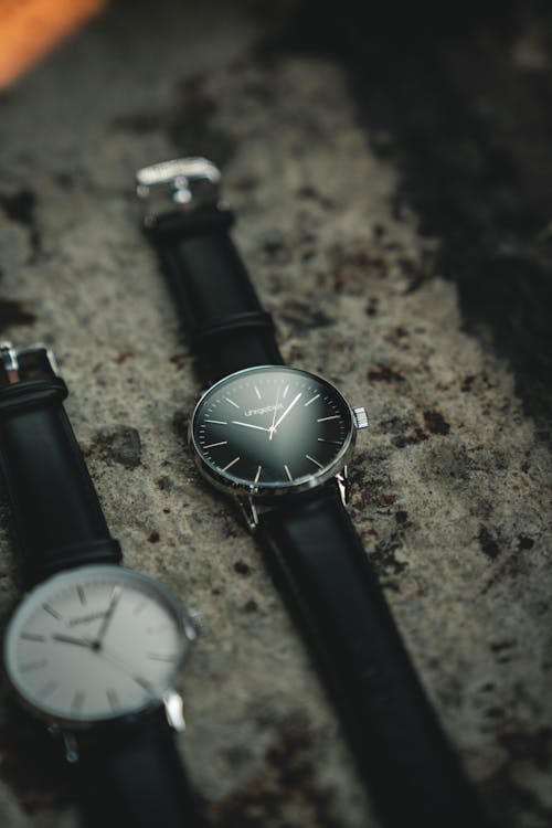 Kostenlos Foto Von Zwei Analogen Uhren Mit Schwarzen Lederbändern Auf Grauer Oberfläche Stock-Foto