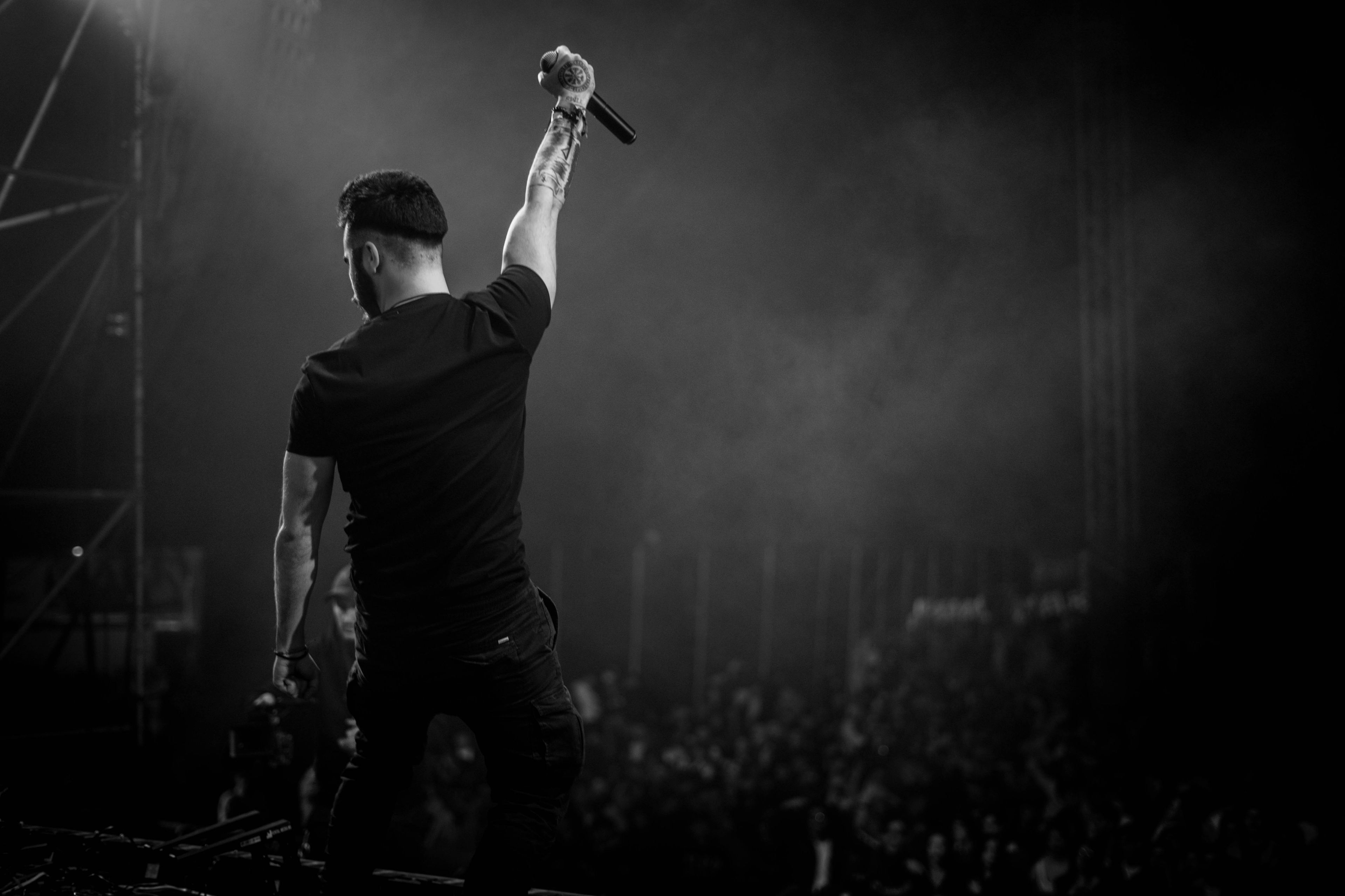 A performer photographed from behind, arm raised to a lit crowd