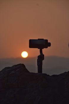 Silhouette of a smartphone on a tripod capturing a stunning mountain sunset.