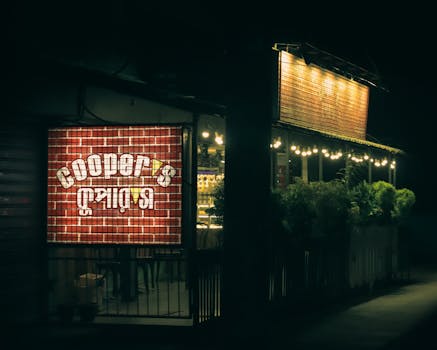 A cozy urban diner illuminated at night with a glowing exterior sign and patio lights.