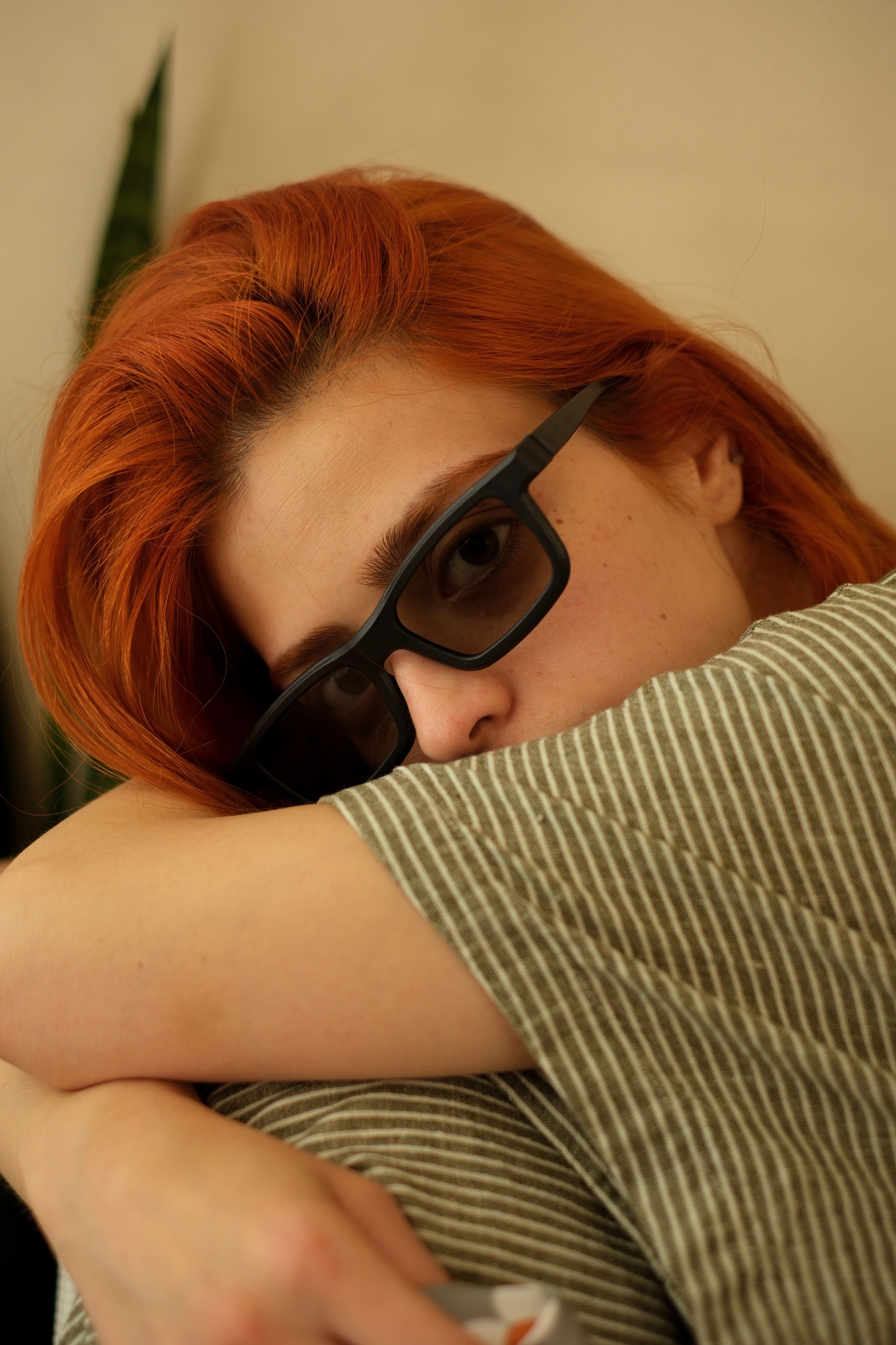 Portrait of a red-haired woman wearing sunglasses. Relaxed indoors setting with a stylish vibe.
