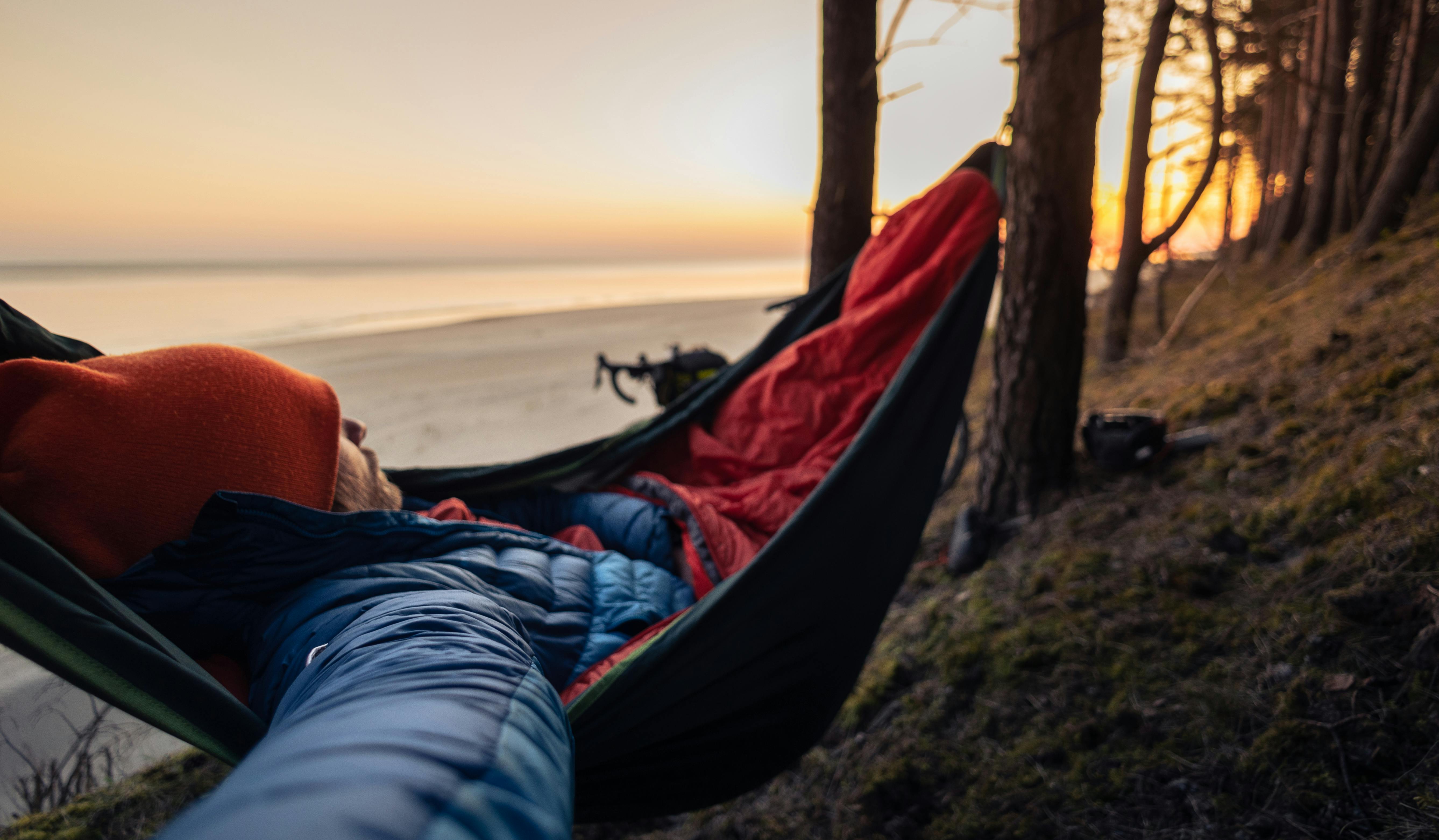 Free Person sleeping in hammock on forested beach at sunset, enjoying outdoor leisure. Stock Photo