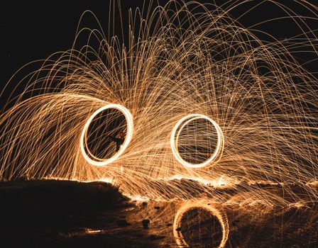 Long exposure of steel wool light painting, creating mesmerizing circular sparks at night.