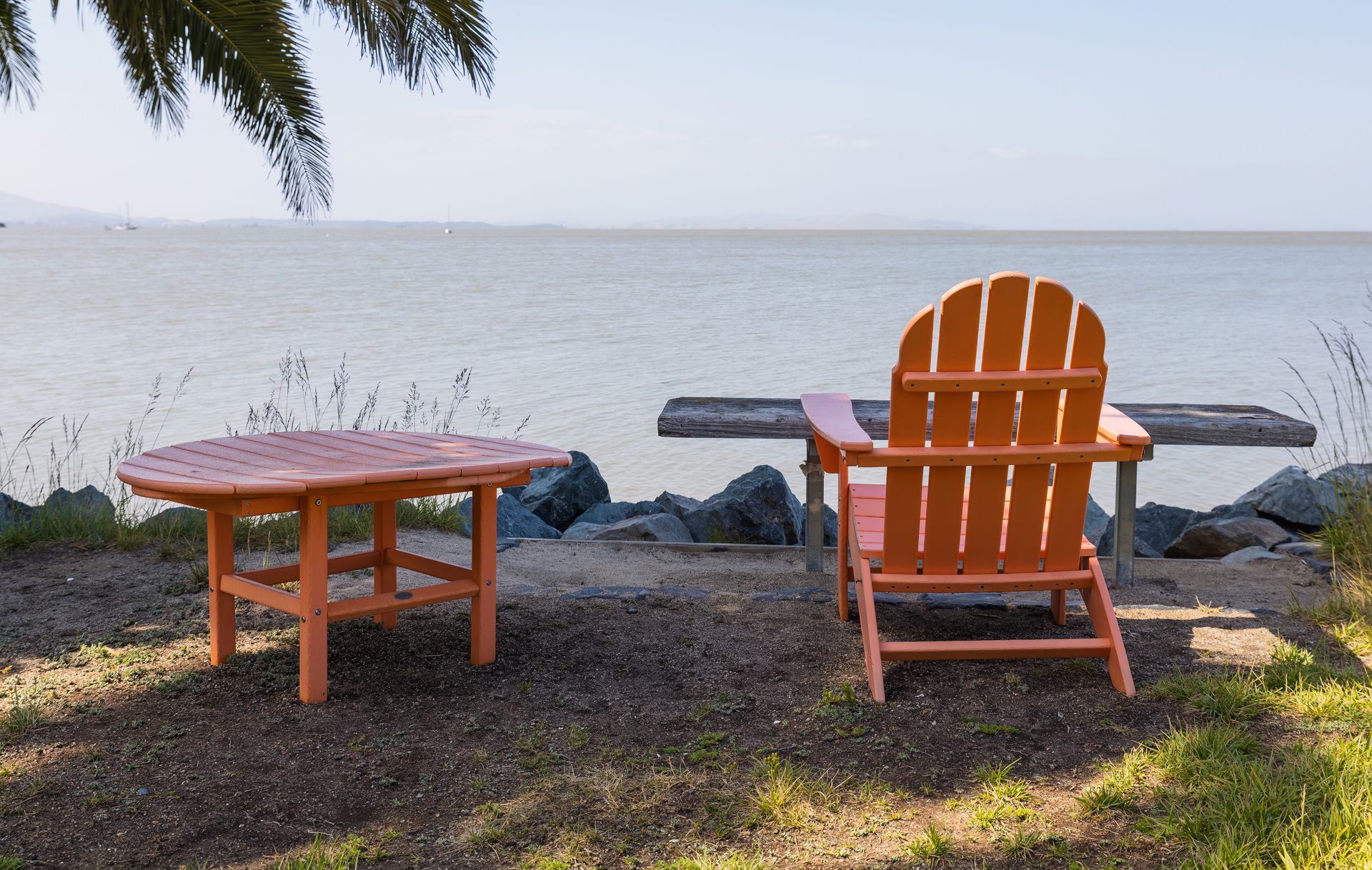 Idyllic lakeside scene with orange Adirondack chair and table, perfect for relaxation.