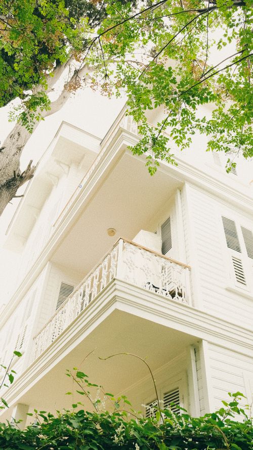 Free Lovely white facade of a residential building with balconies and lush greenery around. Stock Photo