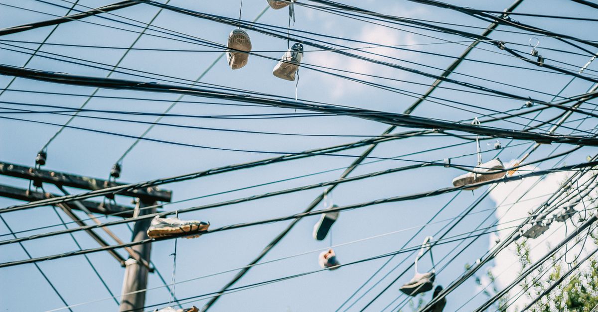 Multiple pairs of shoes hanging from utility wires against a clear blue sky.