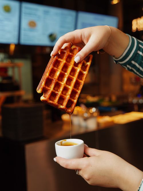 Free Tasty waffle being dipped in syrup at a café, showcasing a delicious breakfast scene. Stock Photo