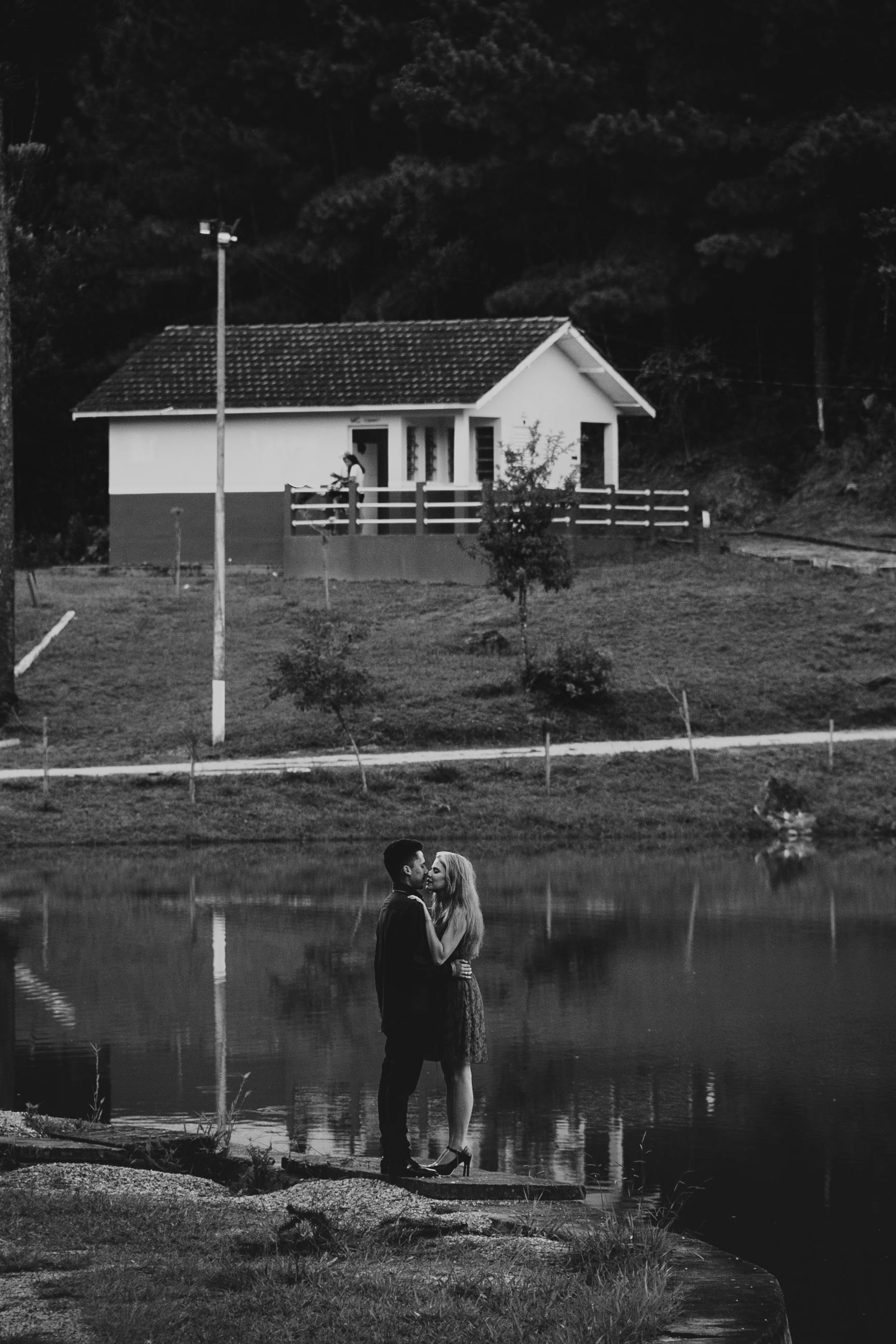 A couple lovingly embraces near a serene lake and house in Curitiba, Brazil.
