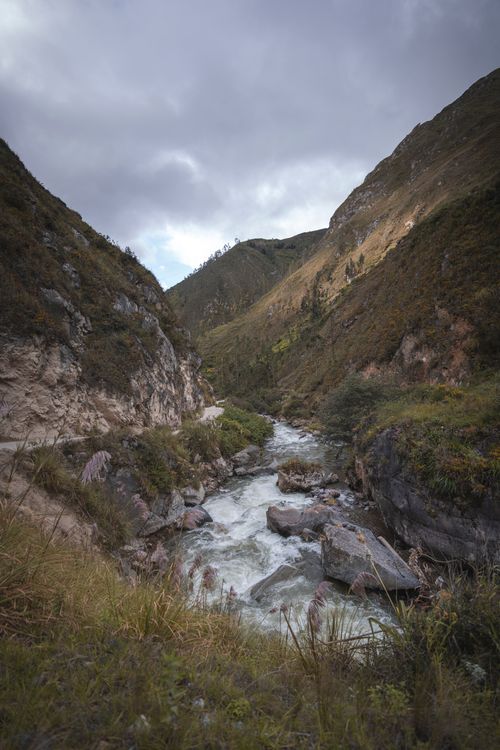 Free Dramatic view of a flowing river in a lush valley surrounded by hills under a cloudy sky in Tarma, Junín, Peru. Stock Photo