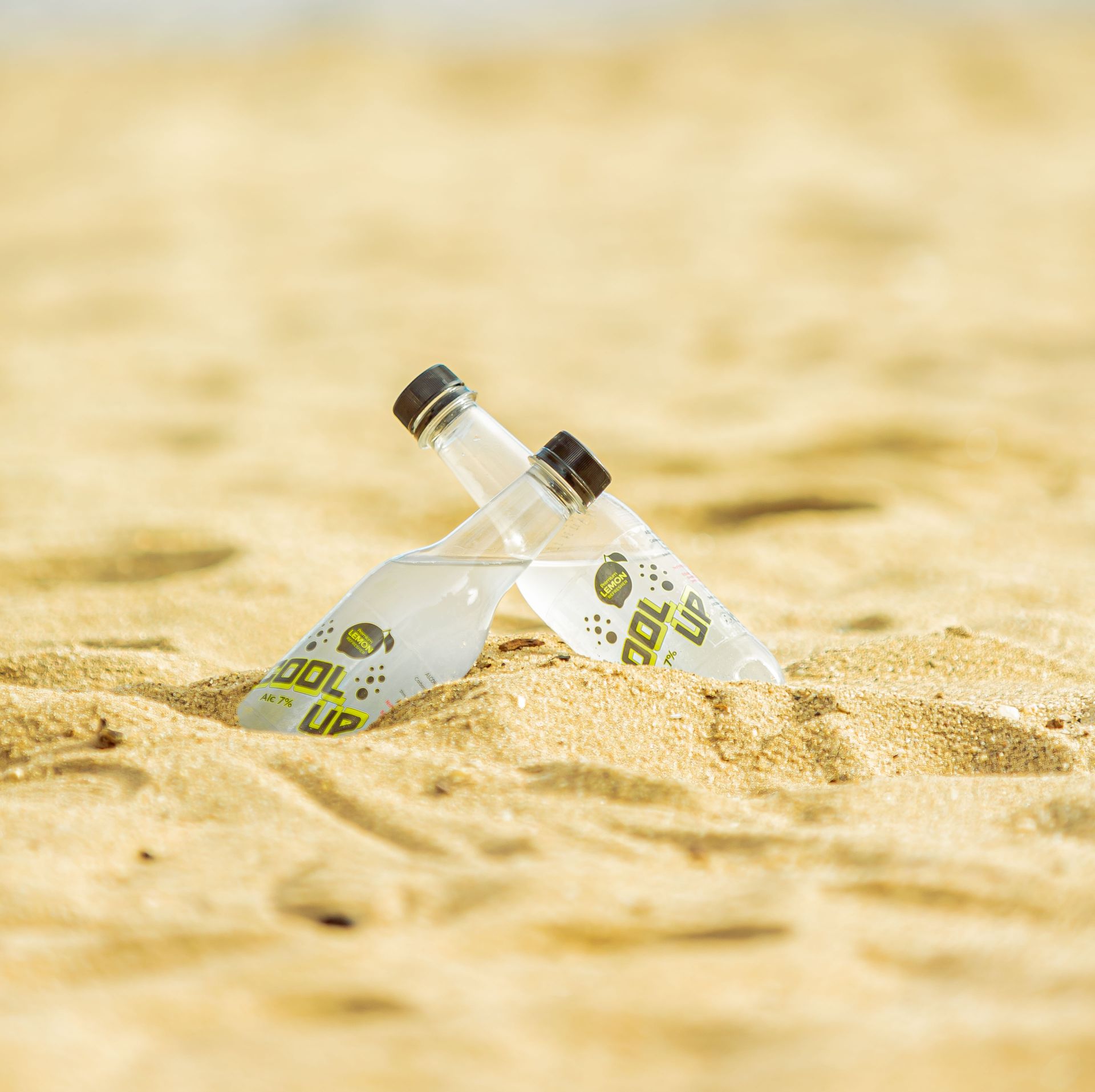 Two glass soda bottles partially buried in sand on a sunny beach.