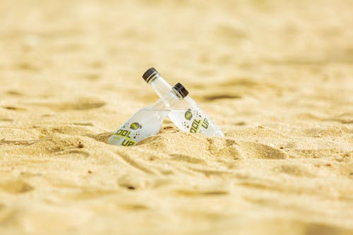 Two Glass Bottles with Drinks in the Sand