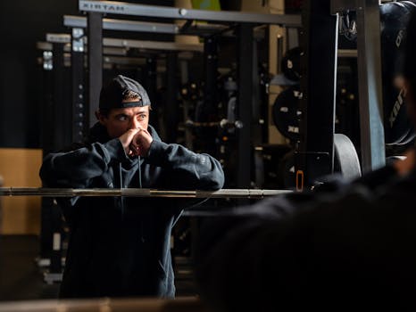 Young male athlete in a gym resting by a barbell, deep in thought. Dramatic lighting enhances the focus.