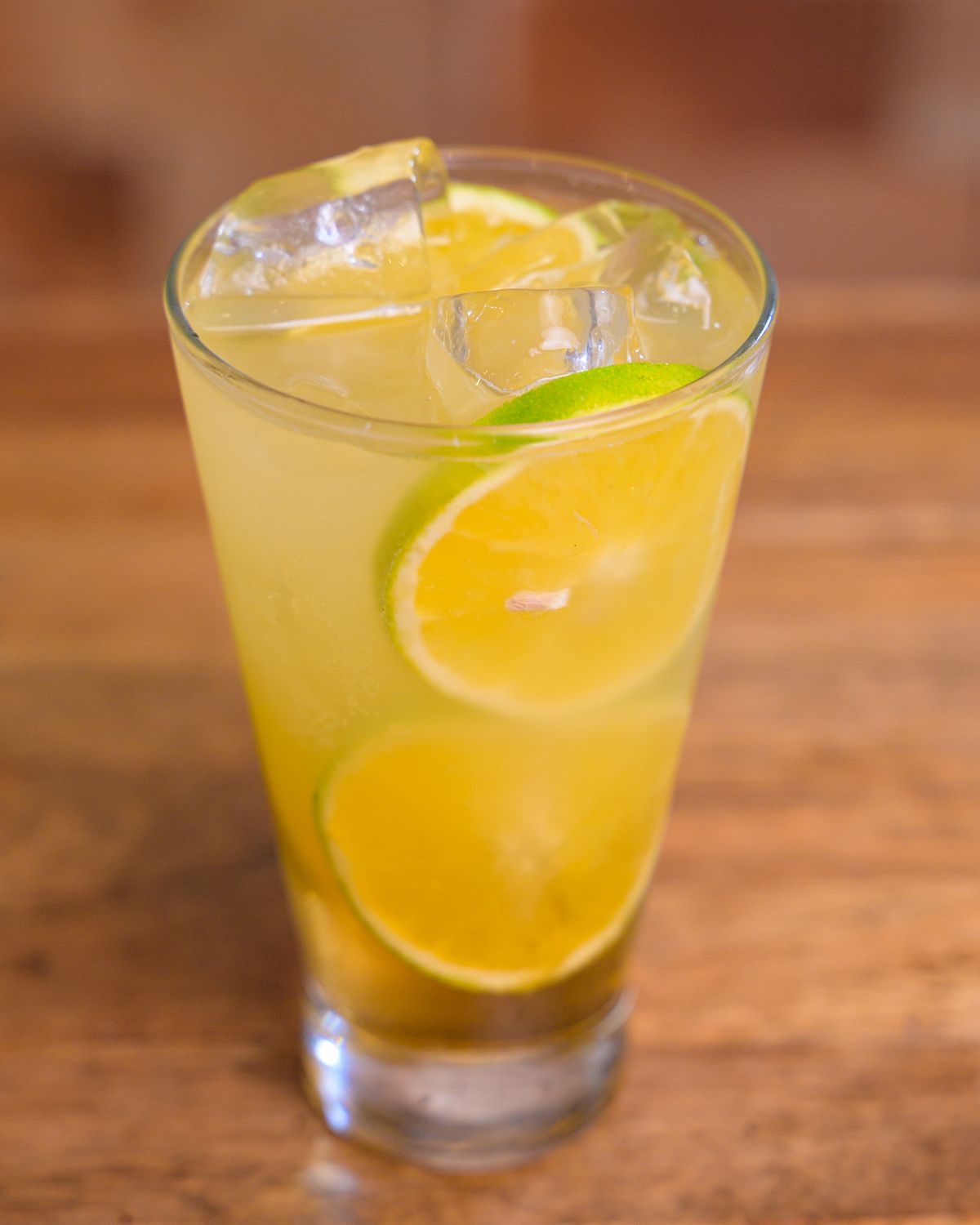 Tall glass of golden limeade with ice cubes and thin lime wheels floating inside