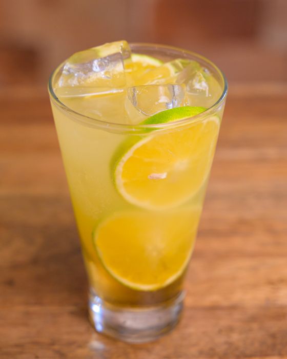Tall glass of golden limeade with ice cubes and thin lime wheels floating inside