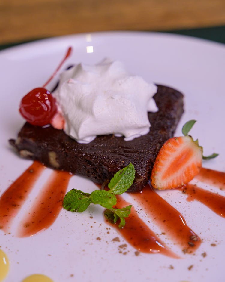 Slice Of Chocolate Cake With Whipped Cream Topping Decorated With Strawberry And Cherry