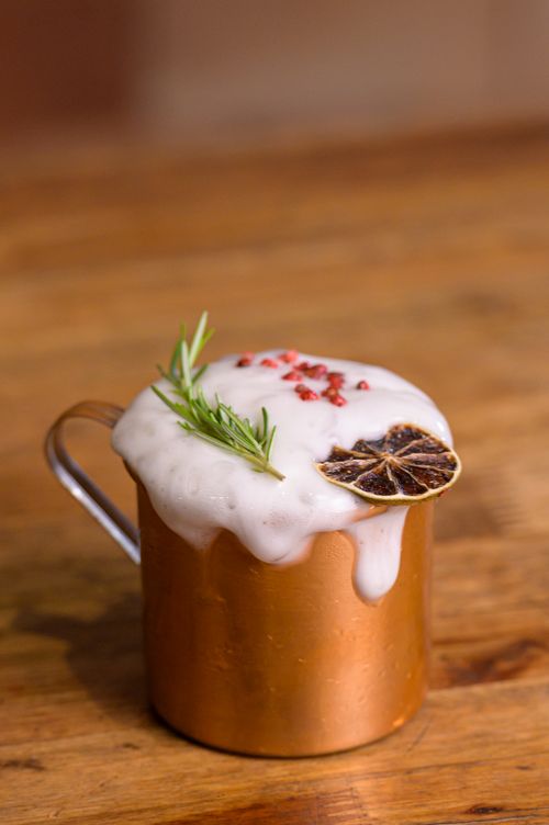 Free A foamy cocktail served in a copper mug adorned with rosemary and dried citrus on a wooden table. Stock Photo