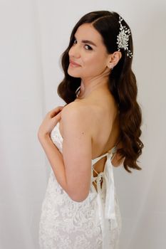 A beautiful bride in a lace wedding dress poses elegantly with a subtle smile and floral headpiece.