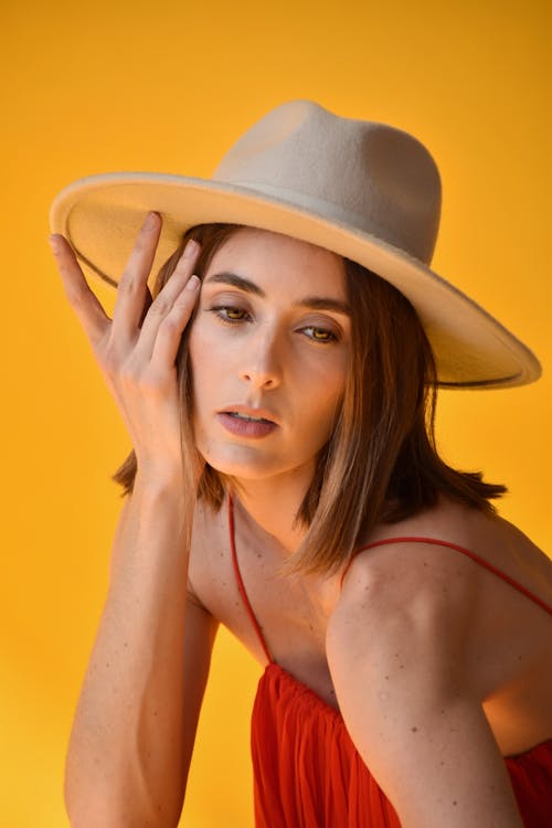 Young Woman in a Dress and Hat Posing in Studio on Yellow Background 