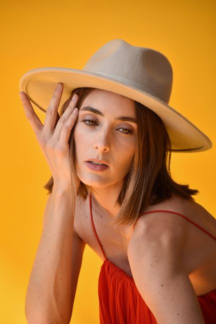 Elegant portrait of a woman wearing a hat against a vibrant yellow backdrop.
