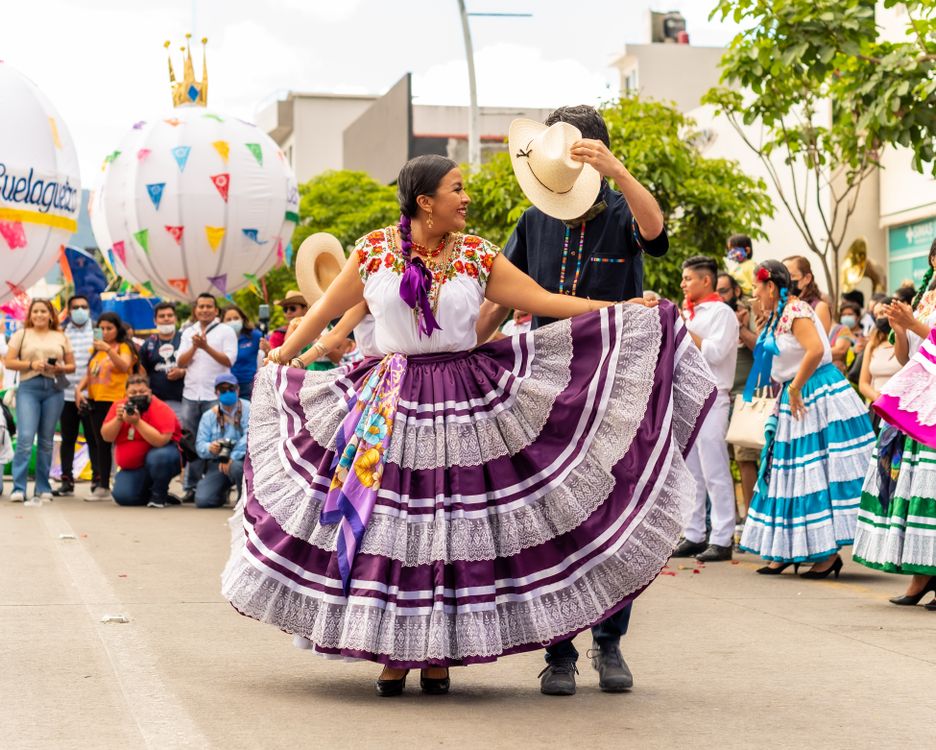 Tänzer in traditionellen bestickten Kostümen feiern das Guelaguetza-Festival in einem farbenfrohen Straßenumzug in Oaxaca Mexiko
