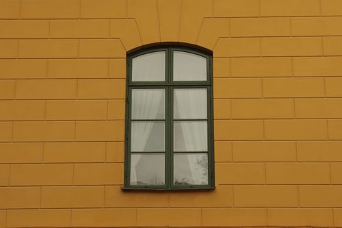 Free Close-up of a yellow building facade with a green arched window in Jönköping, Sweden. Stock Photo
