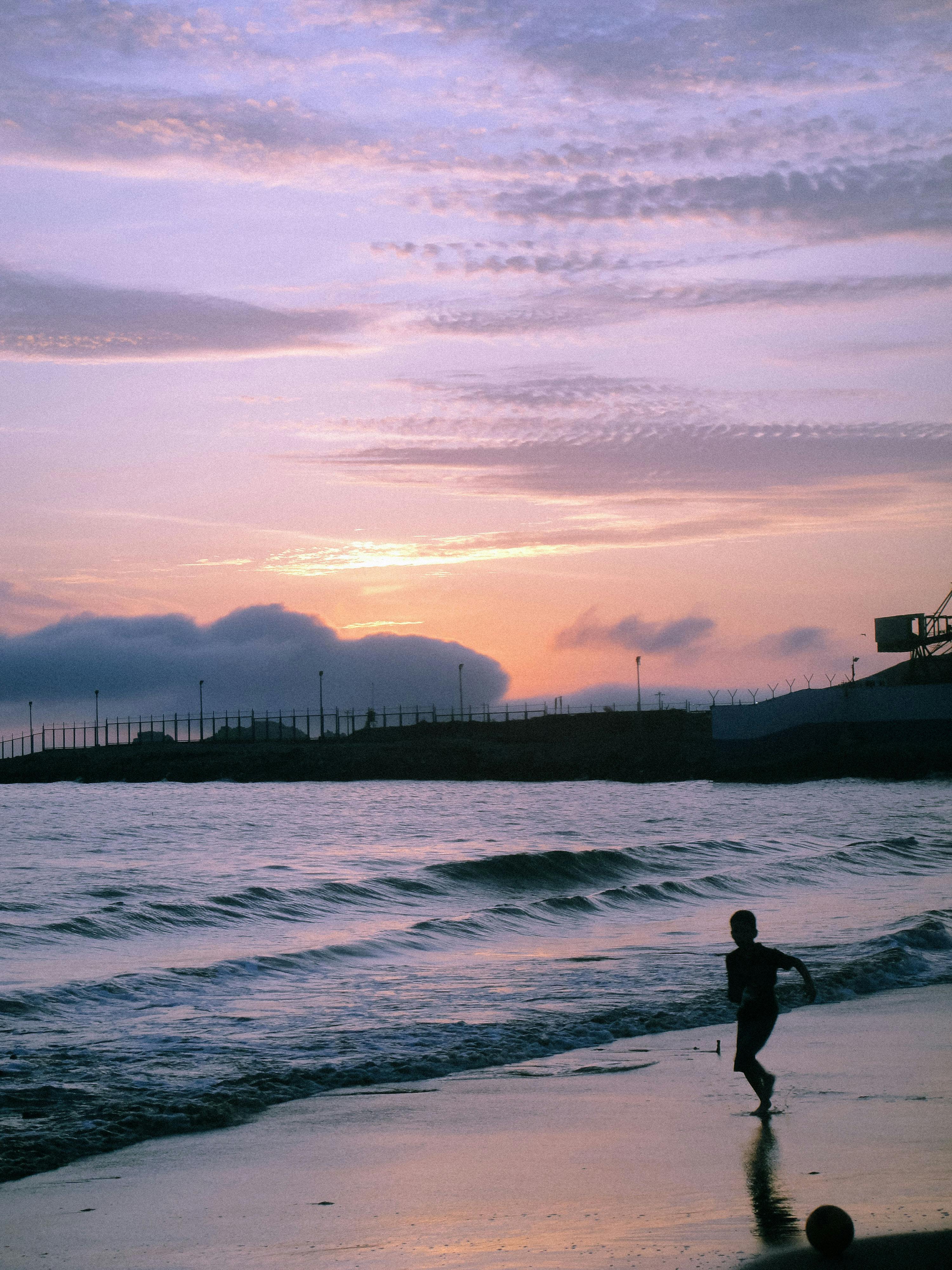 Silhouette of a child playing soccer at sunset on a beach in Chimbote, Perú, with beautiful waves and sky.