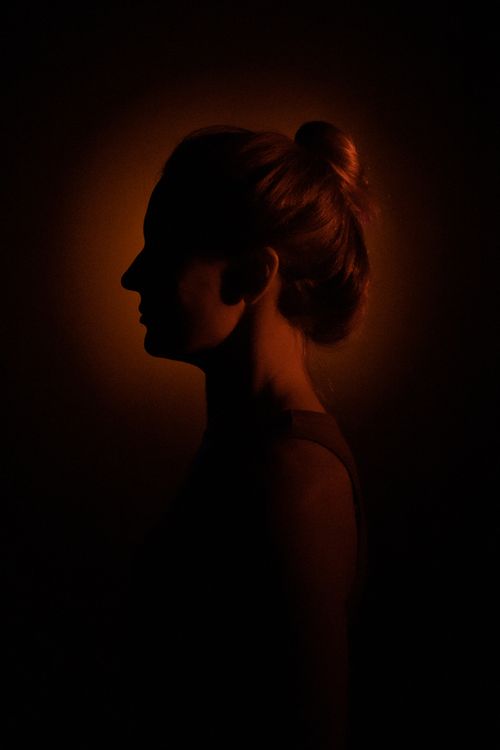 Free Artistic studio portrait capturing a woman's silhouette with dramatic lighting and a warm halo effect. Stock Photo