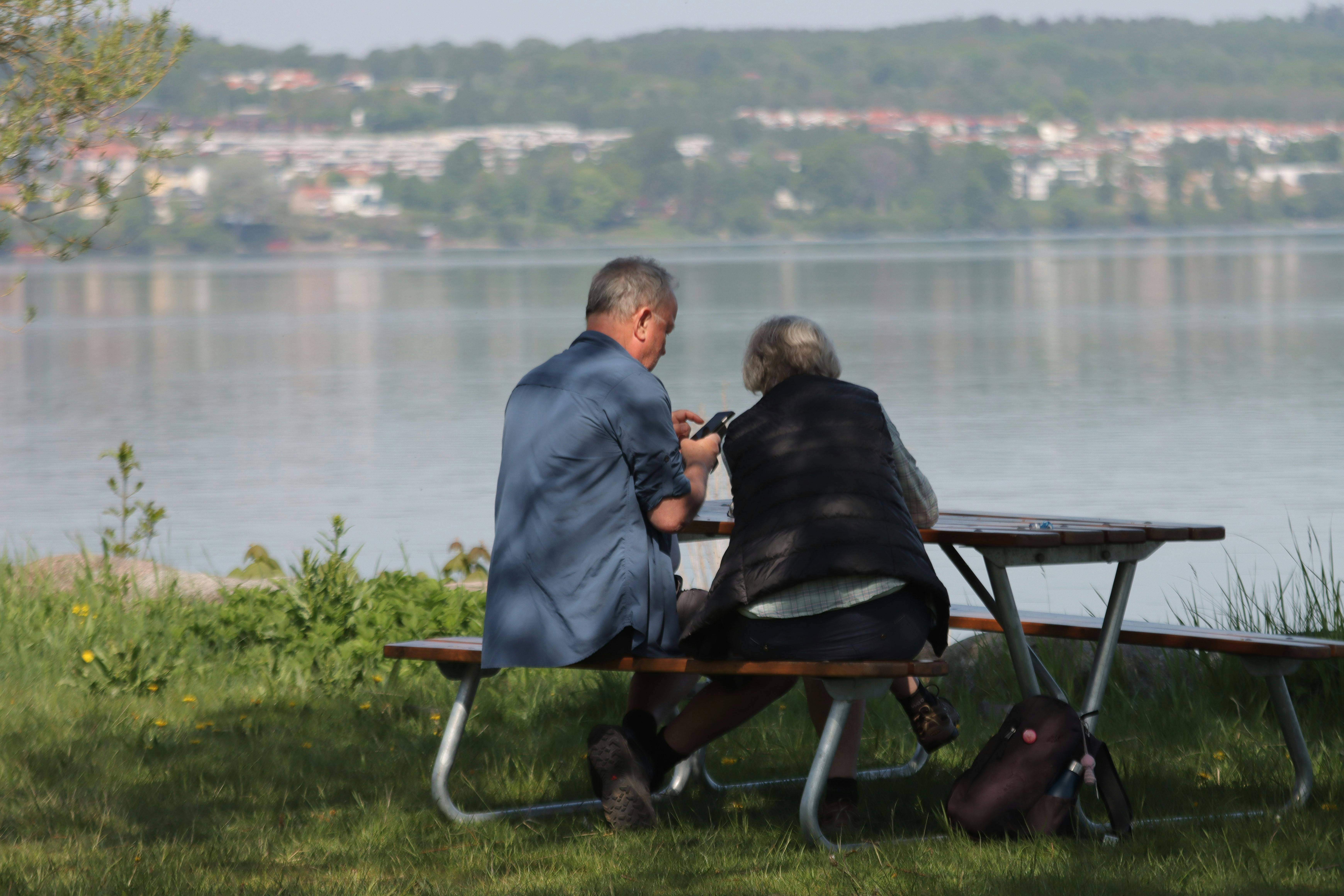 A couple sits at a picnic table by a serene lake in Jönköping, enjoying the peaceful rural scenery.
