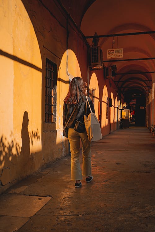 Free Back View of a Young Woman Walking under an Arcade in City  Stock Photo