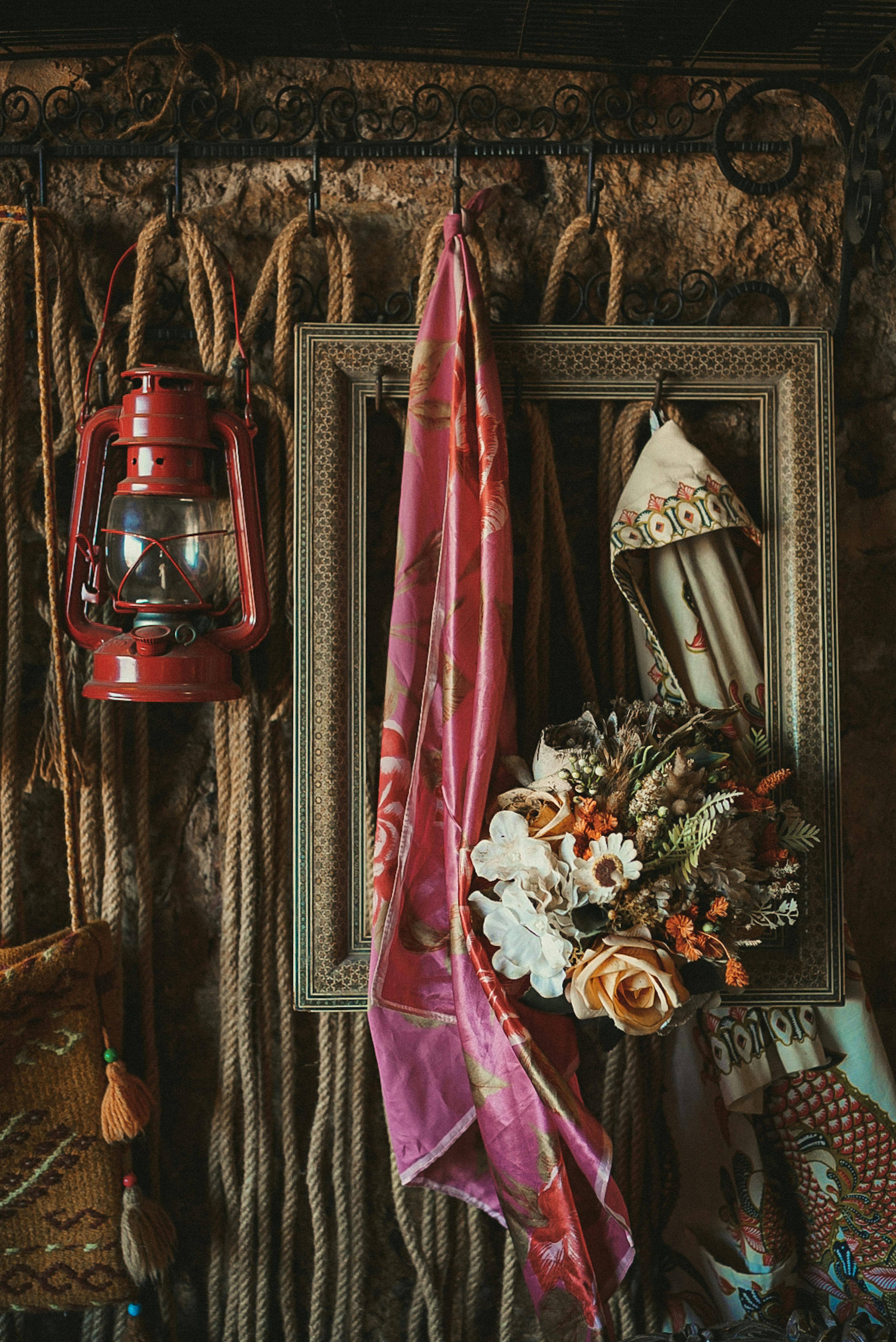 A close-up of vintage decor featuring a lantern, frame, ropes, and floral arrangement.