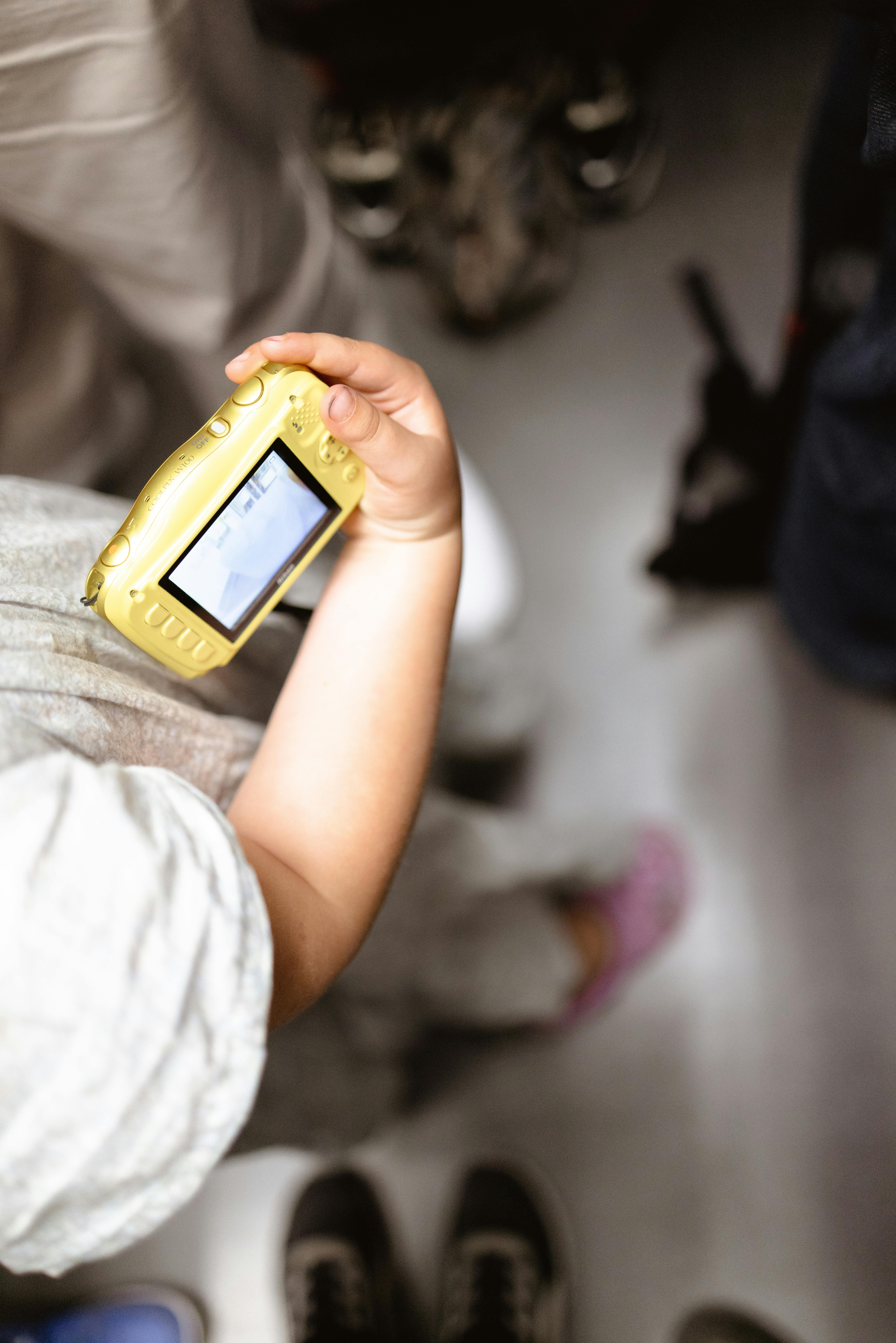 A child's hand holding a yellow digital camera in a crowded space.