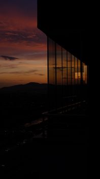 Silhouette of a modern urban building against a vibrant sunset sky, reflecting city views.