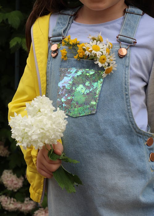 A Little Girl Holding Flowers in Hand and in the Pocket of Her Overalls 