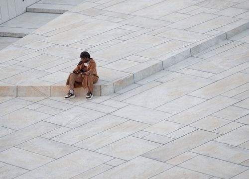 Free A woman sits alone on geometric paved steps in an urban environment, using her smartphone. Stock Photo