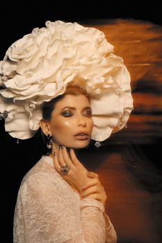 Artistic portrait of a woman wearing a large white floral hat, with glam makeup.