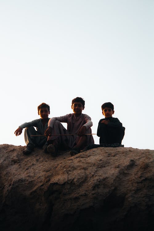 Silhouette of Boys Sitting on a Rock 