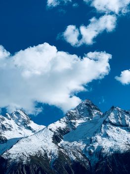 Scenic view of snow-covered mountain peaks in Leh under a bright, clear blue sky with clouds.