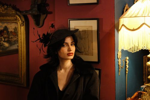 Free Elegant woman in vintage attire poses with hat and veil in a warmly lit room. Stock Photo