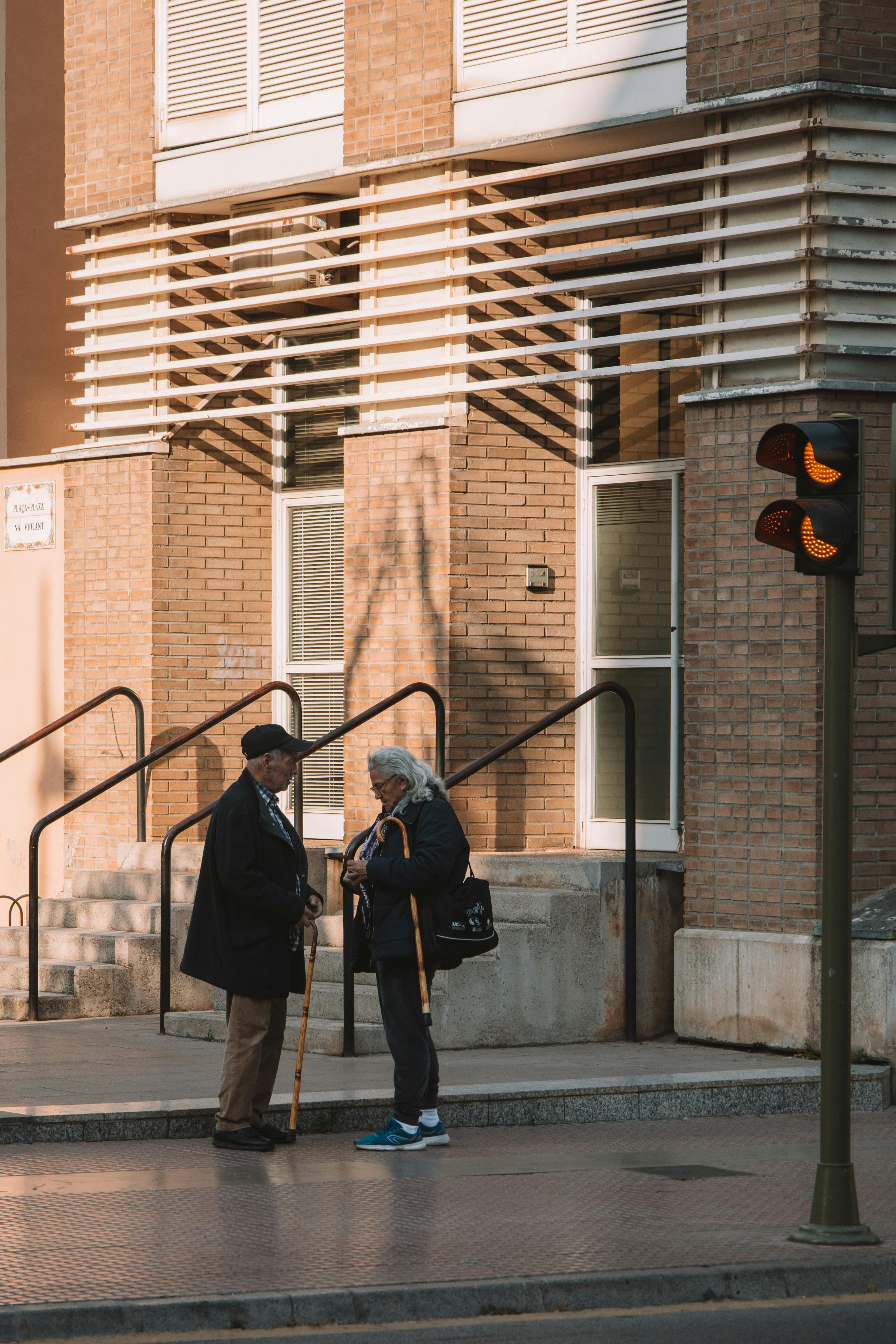 Senior couple chatting on a Valencia sidewalk by a residential building, bathed in warm daylight.
