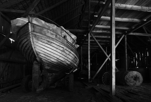 Free A black and white photo of a wooden boat stored inside a rustic barn. Stock Photo