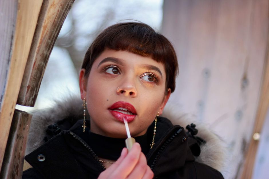 A young woman with red lips applying lipstick outdoors in winter. Fashionable portrait.