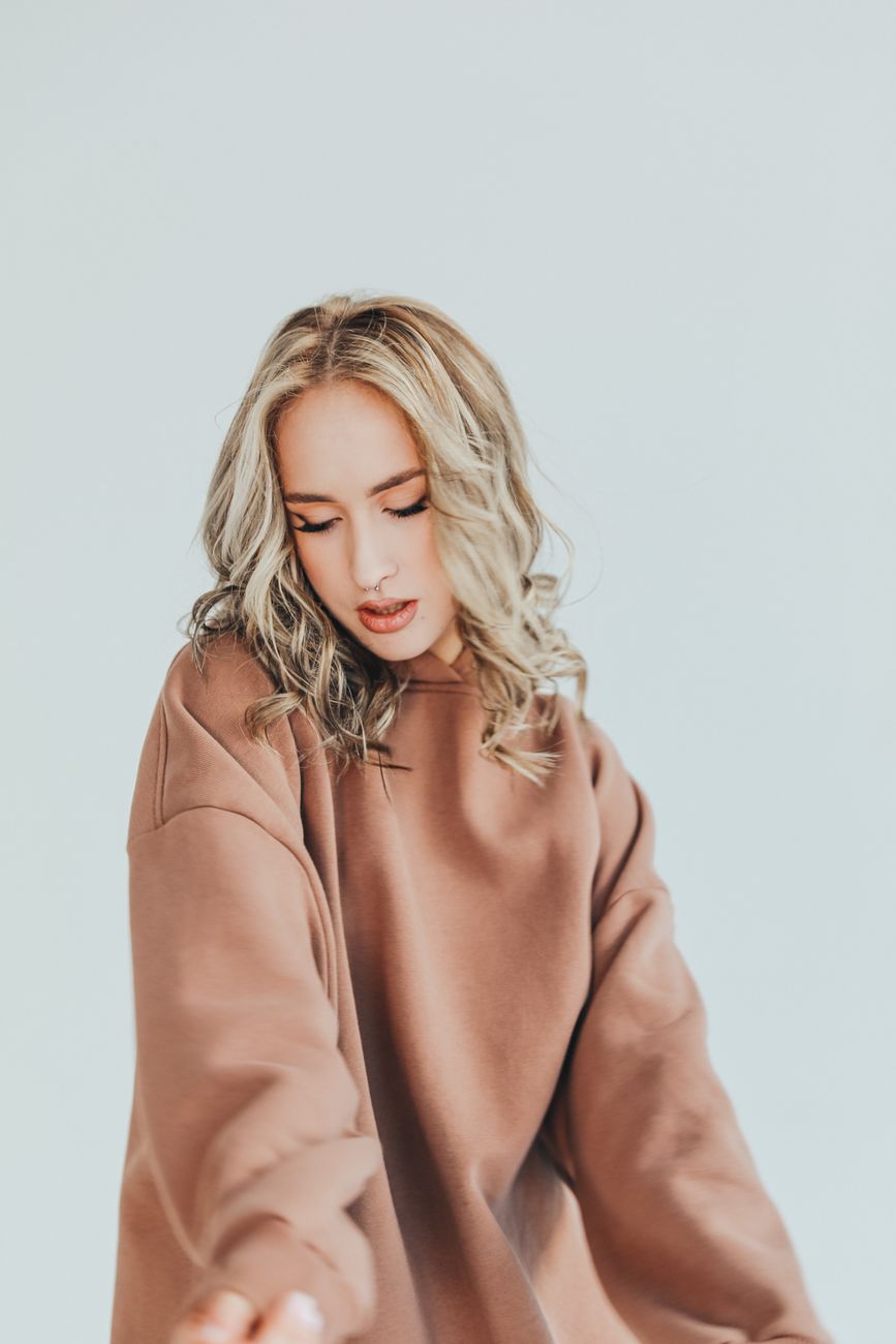 Fashionable woman with blonde hair in a cozy brown hoodie posing against a soft background.