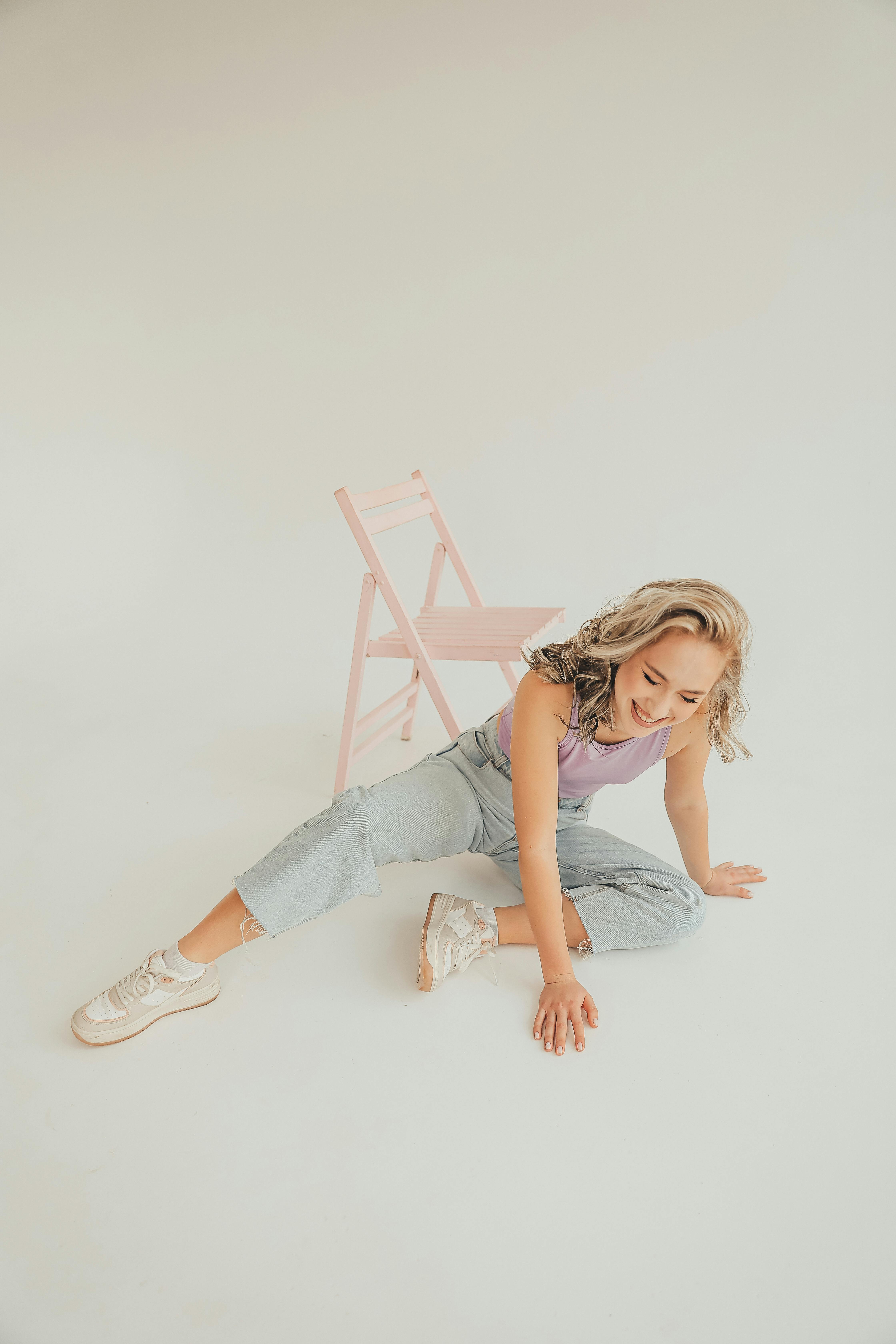Free A blonde woman in jeans and pastel top casually seated in a studio setting, exuding a laid-back vibe. Stock Photo